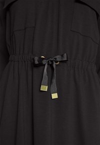 Black dress with short sleeves, featuring a drawstring waist, gold hardware accents, and smooth fabric texture.