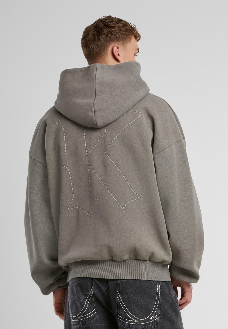 Gray hoodie with a large, stitched letter "K" on the back. Features a drawstring hood and ribbed hem. Fabric has a soft texture.