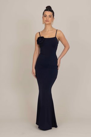 Navy blue sleeveless iltapuku, jossa on tiukka bodice ja levenevä alaosa, ja jossa on kukkakoriste yhdellä olkapäällä. Sujuva rakenne.