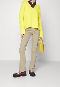 Yellow ribbed knit sweater, brown top, beige pants, and chunky brown boots with black soles. Holding a small yellow handbag.