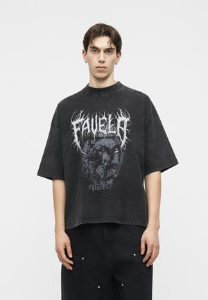 Ung mand med kort mørkt hår iført en overdimensioneret sort grafisk T-shirt og sorte bukser mod en ensfarvet hvid baggrund.