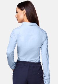 Light blue long-sleeve shirt with a pointed collar and button cuffs, featuring a smooth texture and a relaxed fit, paired with navy pants.