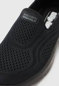 Čierne tenisky Skechers Go Walk s vrchnou časťou z textilu, obsahujúce perforácie, polstrovanú podrážku a dizajn na obúvanie. Protišmyková textúra.