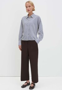 Blau-weiß gestreiftes Hemd zum Knöpfen, braune weite Hose und schwarze flache Schuhe. Das Hemd hat einen Kragen und lange Ärmel.