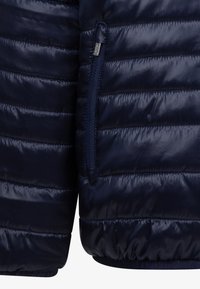 Ναυτικό μπλε μπουφάν puffer με κατακόρυφες ραφές, φερμουάρ πλαϊνές τσέπες και ελαστικό στρίφωμα. Λείο, γυαλιστερό υλικό με ελαφρύ μονωτικό υλικό.
