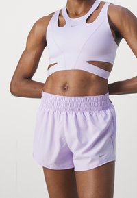 Sostén deportivo lila con diseño recortado y tirantes anchos, combinado con pantalones cortos lila a juego con cintura elástica y logo discreto.