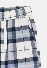 Blaue, weiße und beige karierte Hosen mit einem elastischen Bund, weißem Kordelzug und Seitentaschen auf einem weißen Hintergrund.