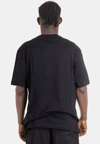 T-shirt nera oversize in cotone. Presenta un colletto a girocollo e maniche corte. Design semplice, senza p pattern o elementi hardware visibili.