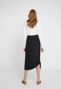 Svart satin midi kjol med en sidöppning och rynkdetalj, tillsammans med en figurnära vit långärmad topp. Mjuk textur och elegant design.