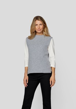 Grauer, gestrickter ärmelloser Oberteil mit hohem Kragen, kombiniert mit weißen langen Ärmeln. Schwarze Hose rundet das Outfit ab. Minimalistisches Design.