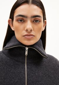 Heren sweater in antracietgrijs met hoge hals van zachte stof, voorzien van een zilveren rits aan de voorkant en geribbelde details op de kraag.