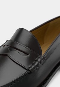 Μαύρα δερμάτινα μοκασίνια με κομψό, γυαλιστερό φινίρισμα, με λεπτομερείς ραφές και διακοσμητική ταινία στο μπροστινό μέρος. Λείο εσωτερικό επένδυση.