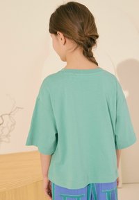 Türkises T-Shirt mit kurzen Ärmeln aus weichem Baumwollstoff, mit runder Ausschnitt und lässiger Passform. Die Rückansicht zeigt die glatte Textur und die Nähdetails.