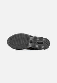 Black running shoe sole with textured grip pattern, featuring multiple grooves, circular accents, and a layered design for flexibility.