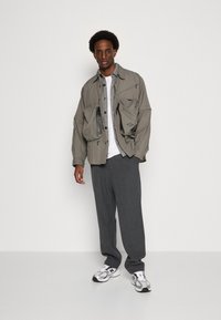 Light gray, oversized, nylon jacket with multiple pockets and buttons, paired with gray plaid pants and white sneakers with black accents.
