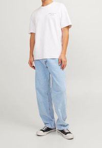 Camiseta blanca de algodón de manga corta, con un pequeño logo impreso; jeans de mezclilla azul claro de corte relajado; zapatillas negras con suelas blancas.