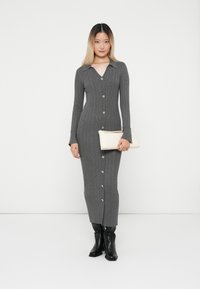 Μακριά, γκρι ριγέ φόρεμα με γιακά, μπροστινά κουμπιά και μακριά μανίκια. Φορεμένο με μαύρες μπότες μέχρι το γόνατο και κρέμ τσάντα χειρός.