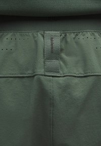 Pantaloni sportivi verdi con una superficie testurizzata, vita elastica e piccoli fori di ventilazione. Presentano un'etichetta cucita nella vita.