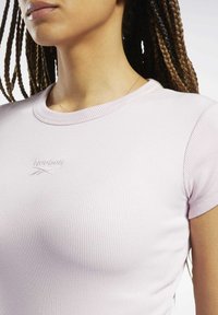 Gaiši rozā ribota īslaiku T-kreklu, kam uz krūtīm ir neliela izšūta Reebok logo. Apkakle ir apaļa un pieguļoša.