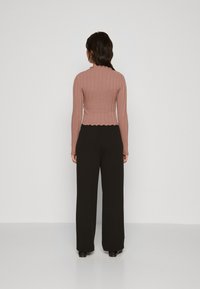 Cotton ribbed top in dusty rose with scalloped hem and long sleeves, paired with high-waisted black wide-leg trousers.