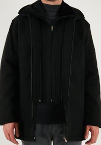 Giacca nera con zip, caratterizzata da un ampio colletto, realizzata in tessuto morbido, con due zip frontali, cordini e una vestibilità rilassata. Fodera interna texturizzata.