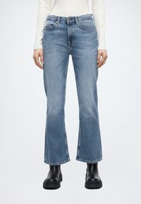 Világos koptatású, farmer anyagból készült kék bővülő szárú farmernadrág, ötzsebes kialakítással, kontrasztos varrással és gombos derékrésszel.