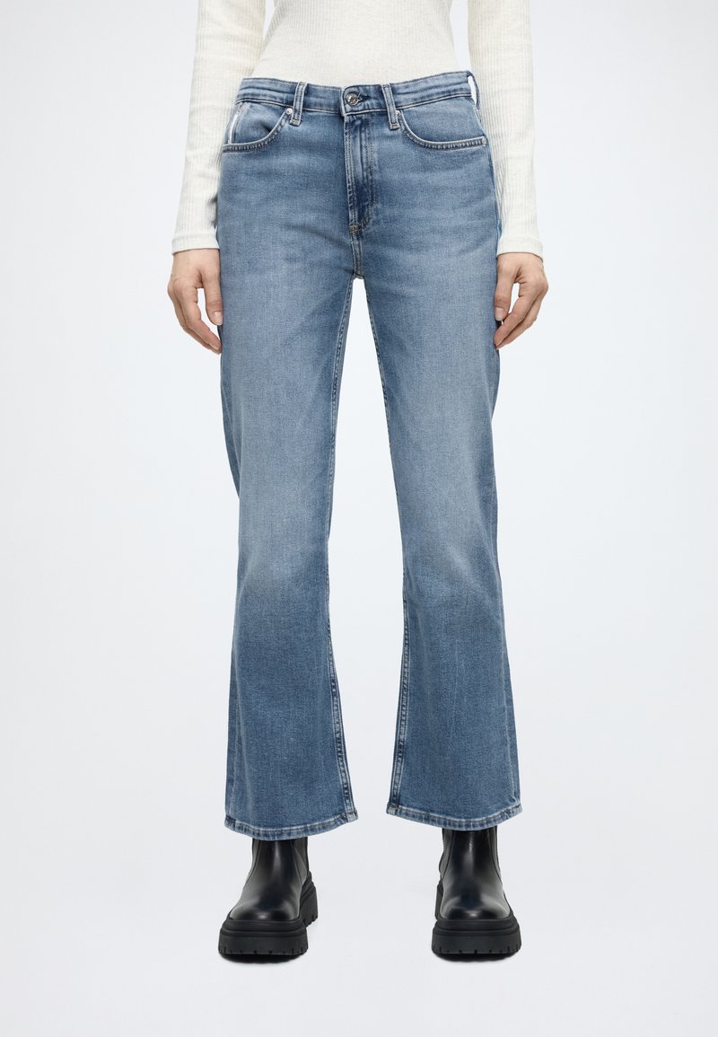 Világos koptatású, farmer anyagból készült kék bővülő szárú farmernadrág, ötzsebes kialakítással, kontrasztos varrással és gombos derékrésszel.