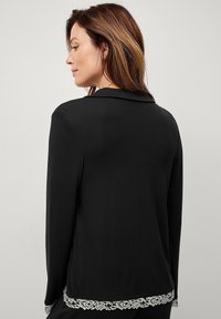 Sort langærmet bluse med krave og blondekant i kanten. Blødt, glat stof med en skræddersyet pasform.