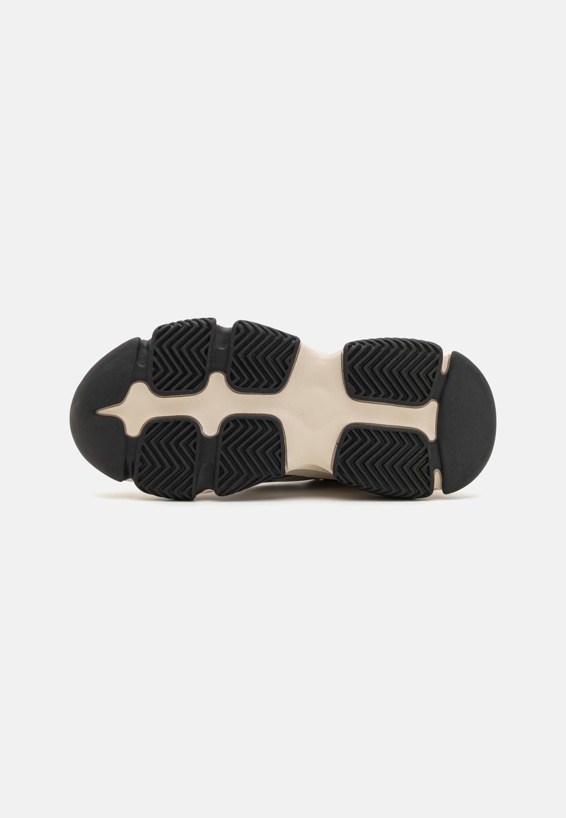 Suela de zapato deportivo en negro y crema con un patrón de goma texturizada, que presenta surcos para tracción y un talón redondeado para soporte.