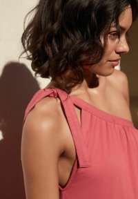 Top senza maniche di colore rosa con un design arricciato, caratterizzato da una spallina legata su una spalla e una texture di tessuto morbido e liscio.