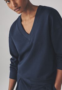 Marineblå v-hals sweatshirt lavet af blødt stof, med ribbede ærmer og kant, i en afslappet pasform og med en subtil tekstur.