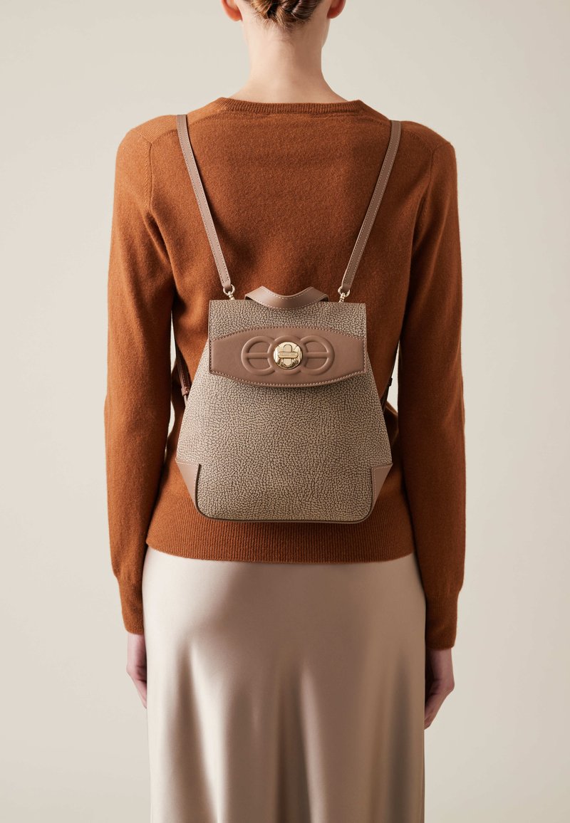Textured leather backpack in beige with brown accents, featuring a rounded flap with a gold clasp and adjustable straps.