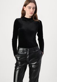 Top en velours noir à manches longues avec col montant, associé à un pantalon en cuir noir brillant doté de poches avant et d'une coupe droite.