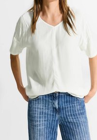 Vit kortärmad topp med V-ringning och en mjuk textur. Parat med blårandiga jeans i denim med fickor och knappstängning.