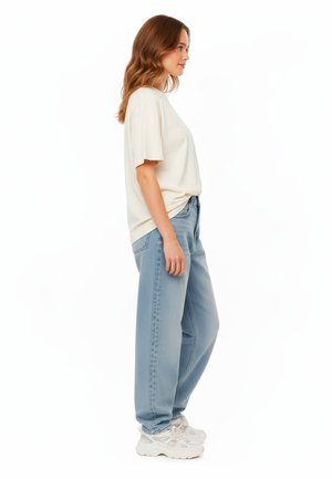 T-shirt loose-fit color beige chiaro abbinato a jeans a vita alta dritti blu chiaro e sneakers bianche e voluminose. Tessuto morbido e design casual.