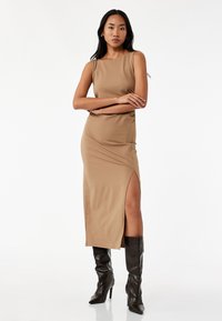 Tan halterneck kjole med en slidse i siden, lavet af glat stof. Bæres med sort knæhøj hæl støvler. Simpelt, tætsiddende design.