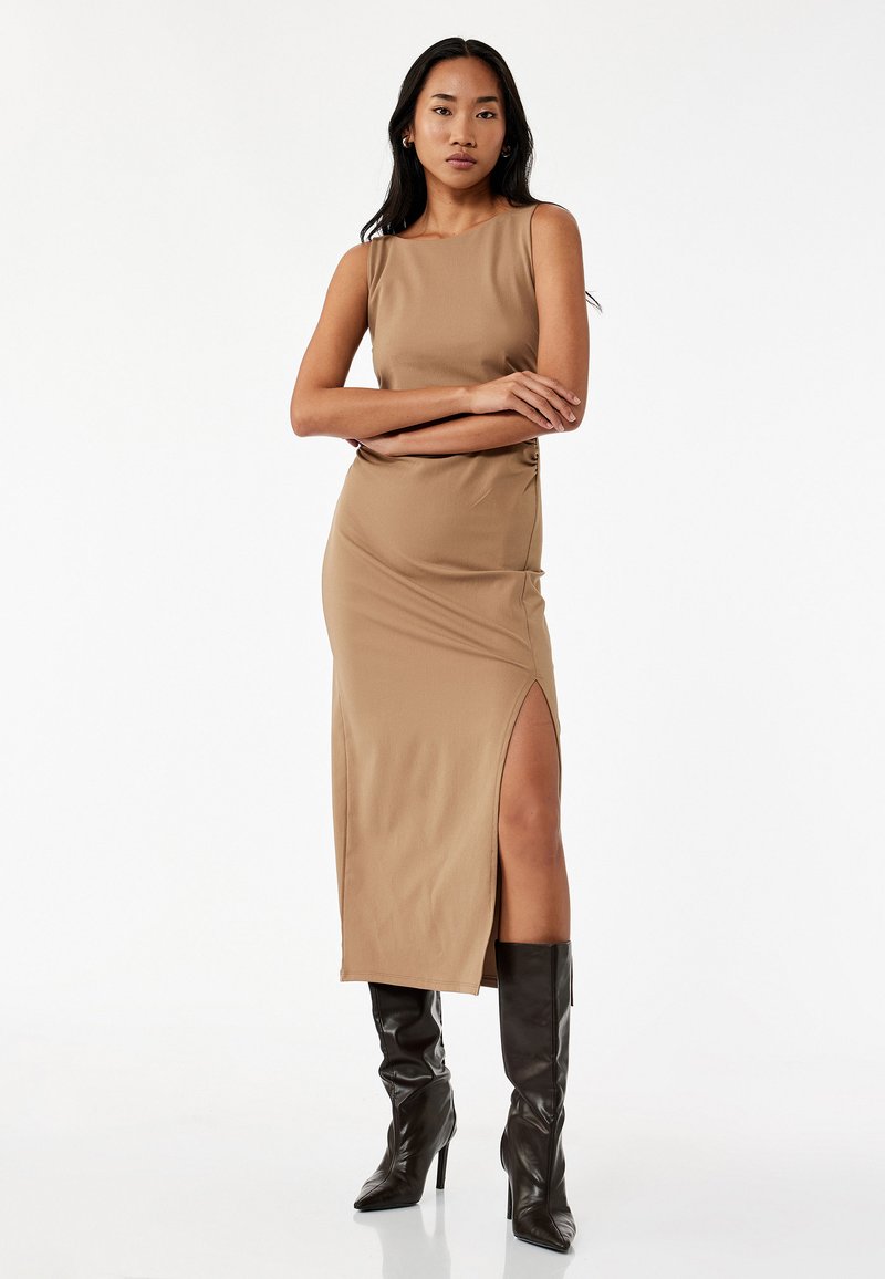 Tan halterneck kjole med en slidse i siden, lavet af glat stof. Bæres med sort knæhøj hæl støvler. Simpelt, tætsiddende design.