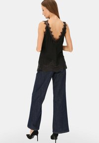 Czarna jedwabna koszulka na ramiączkach z koronkową lamówką wzdłuż dekoltu i dołu, zestawiona z luźnymi, ciemnymi dżinsami i czarnymi wysokimi obcasami.