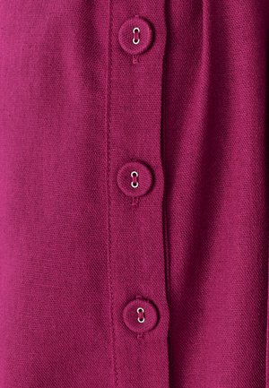 Fuksija audums ar četriem apaļiem pogām, katrai ar metāla cilpu. Tekstūra ir gluda ar adītas izskatu.