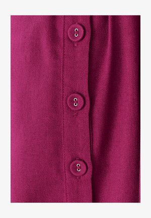 Fuksiaroosa kangas, millel on nelja ümmarguse nupu rida, igal nupul on metallist silmus. Tekstuur on sile ja see näeb välja nagu kudumine.