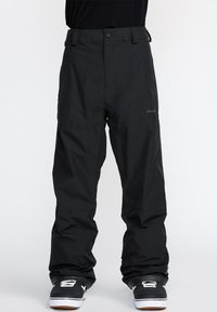Pantalon de snowboard noir avec une coupe ample, fabriqué en matériau imperméable. Il possède des passants de ceinture, une fermeture avec bouton et un logo discret près de l'ourlet.