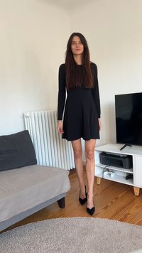 Juoda ilgomis rankovėmis suknelė su aptemptu liemeniu ir praplatėjusia sijonu. Dėvima kartu su juodais smailiais bateliais ant medinių grindų, suteikiančių lygų tekstūros kontrastą.