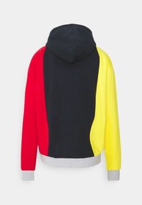 Mikina s kapucí s designem v barevných blocích, která obsahuje červené, černé a žluté části, šedé manžety a lem, vyrobená z měkkého materiálu.