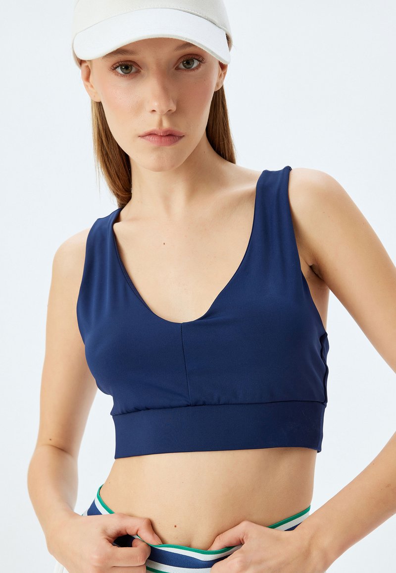 Navy sininen urheilu crop top syvällä V-kaula-aukolla ja saumattomalla viimeistelyllä, valmistettu sileästä ja joustavasta kankaasta, yhdistetty raidalliseen vyötäröosuuteen.