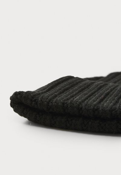 Juodas megztas kepurė su šonkauliniais raštais. Minkšta medžiaga, sulenkta krašto dalis, kompaktiška forma, minimalus dizainas. Tinka šaltam orui.