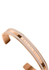 Rožinio aukso metalo apyrankė su dviem lygiagrečiomis juostelėmis, viena glotni, kita graviruota "DANIEL WELLINGTON." Išmanus ir minimalistinis dizainas.