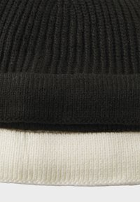 To strikkede beanies stablet oven på hinanden, en sort med ribbet tekstur og en cremefarvet med en glat, tæt vævet finish.
