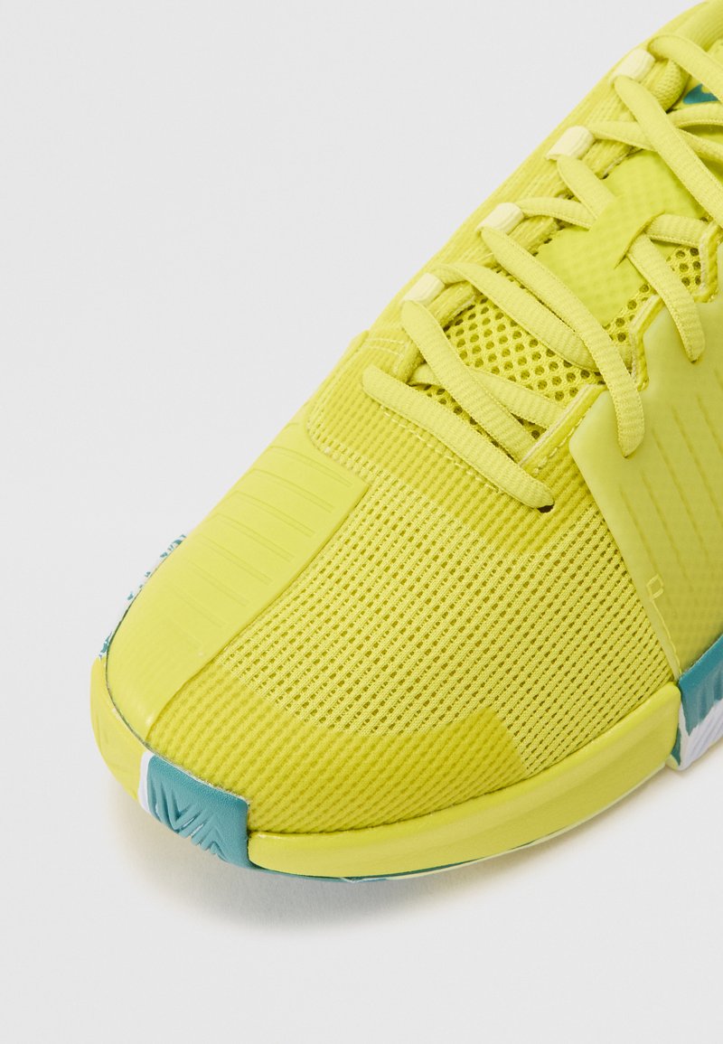 Scarpa da ginnastica gialla con tomaia in rete traspirante, punta rinforzata, dettagli testurizzati e un accento teal sulla suola.