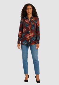 Camicia a maniche lunghe color borgogna con fiori blu e rosa, colletto con bottoni, abbinata a jeans azzurri e tacchi neri.