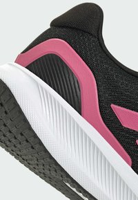 Black athletic shoe with a textured mesh upper, pink accents, and a white rubber sole featuring a tread pattern for grip.
